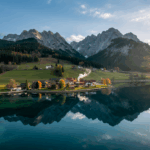 Drohnenaufnahmen Kärnten – malerischer Blick auf eine idyllische Landschaft mit Bergsee und sanften Hügeln im Sonnenlicht.