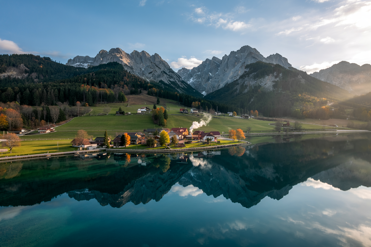 Drohnenaufnahmen Kärnten – malerischer Blick auf eine idyllische Landschaft mit Bergsee und sanften Hügeln im Sonnenlicht.