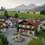 Drohnenaufnahmen Kärnten – Bergdorf in Kärnten inmitten von grünen Wiesen und sanften Hügeln.