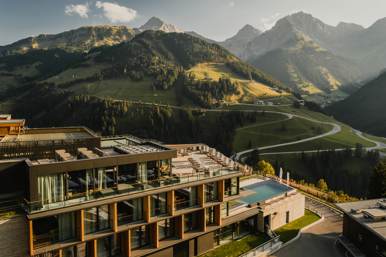 Luxuriöses Hotel in Kärnten mit Panoramablick auf grüne Almen und beeindruckende Berggipfel bei Abendsonne.