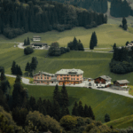 Panoramablick auf Almwiesen und traditionelle Berggasthöfe in Kärnten, umgeben von üppigen Wäldern und sanften Hügeln.