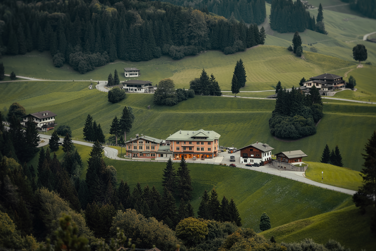 Panoramablick auf Almwiesen und traditionelle Berggasthöfe in Kärnten, umgeben von üppigen Wäldern und sanften Hügeln.